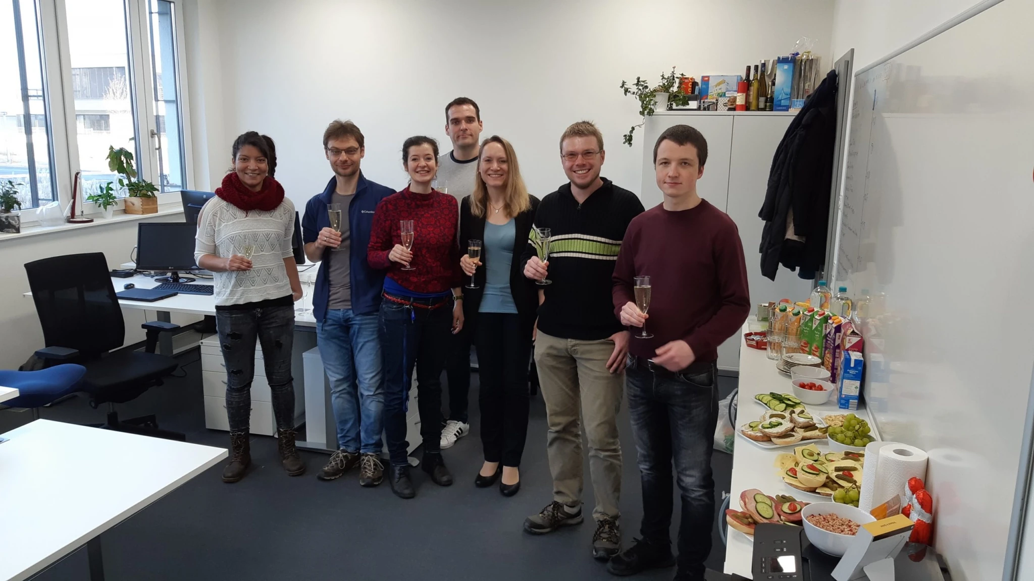 Gruppe von Kolleg:innen im Büro, mit Essen und Getränken auf einem Tisch.