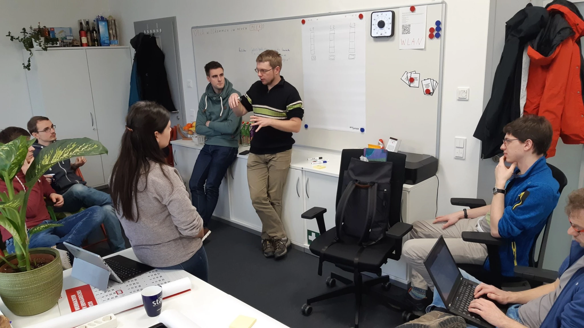 Gruppe von Peerox-Mitarbeitenden diskutiert stehend und sitzend vor einem Whiteboard im Büro.