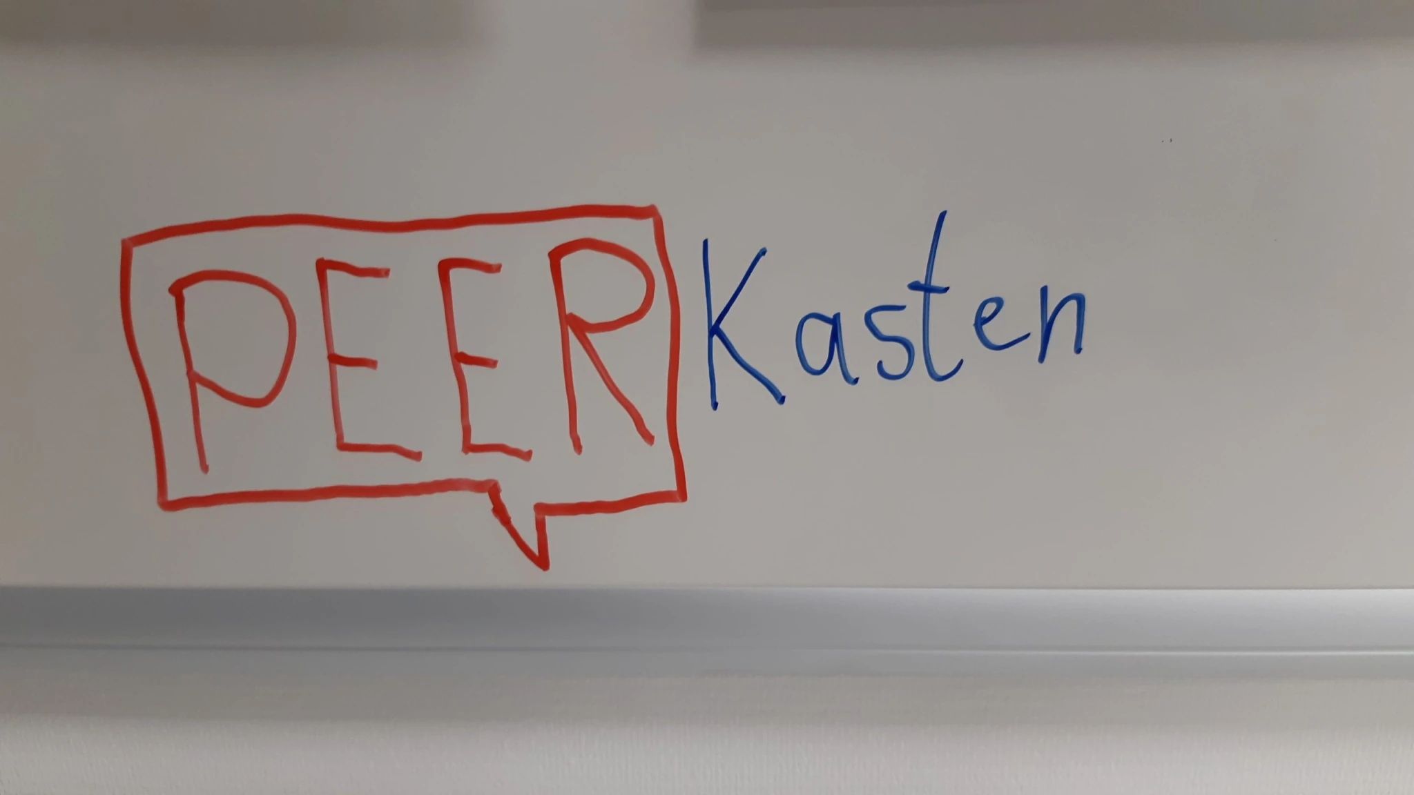 Mit rotem Marker geschriebenes Whiteboard-Logo „PEER Kasten“ im Peerox-Büro.