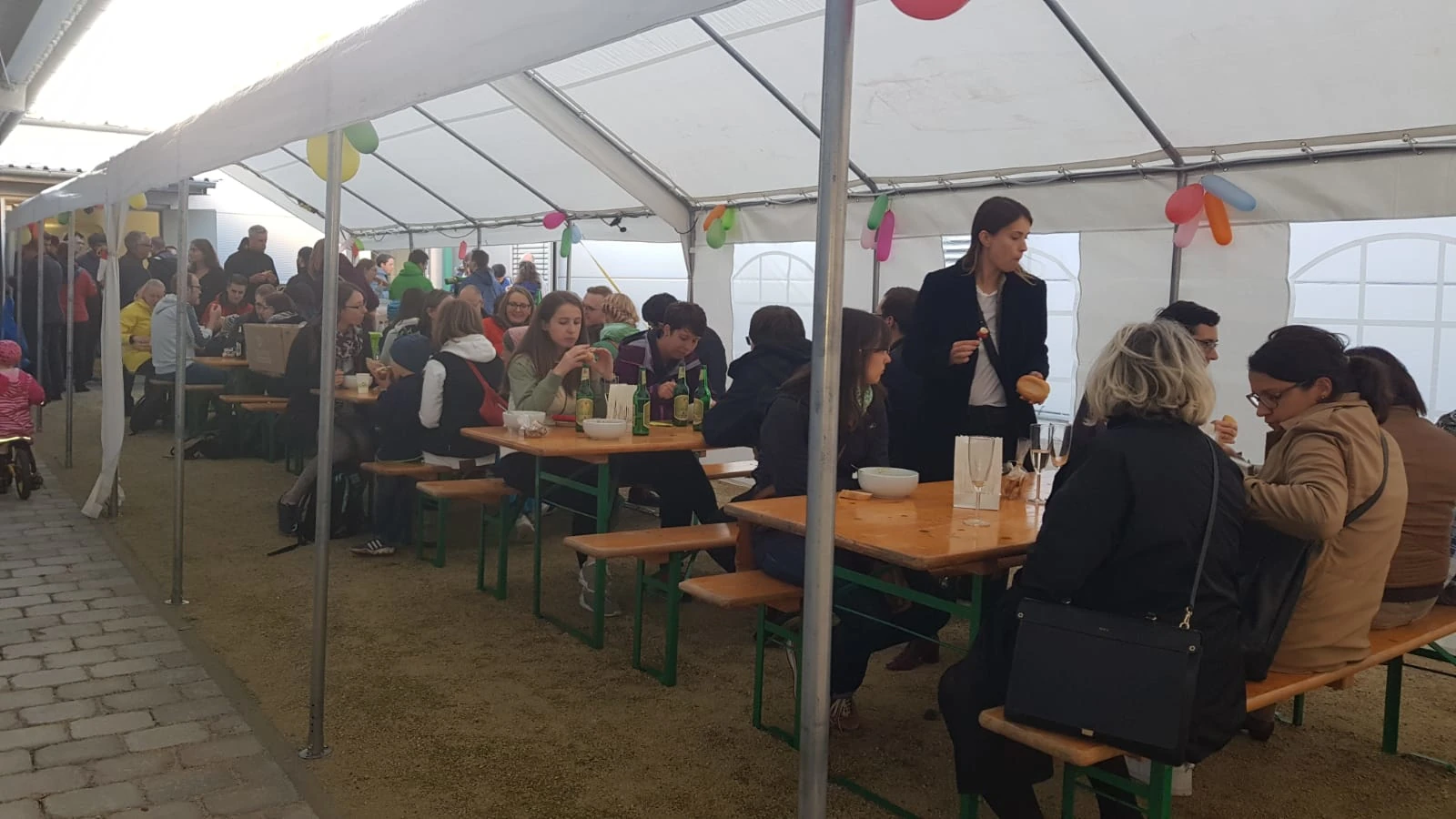Gäste beim Sommerfest im Außenbereich an Biertischen im Gespräch.