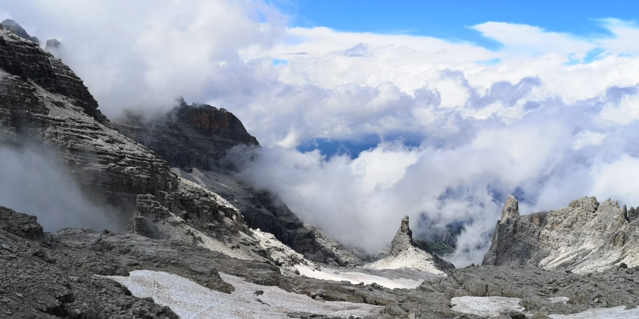 Blick auf felsige Berglandschaft mit Nebelschwaden und Wolken zwischen den Gipfeln.
