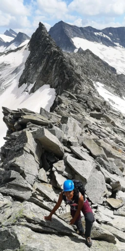 Person steht auf einem felsigen Gipfel mit weitem Blick über das Gebirge.